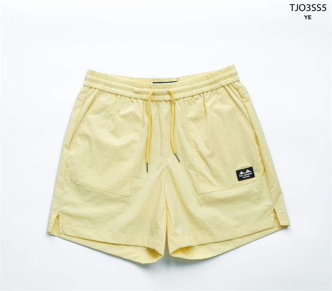 Pale yellow drawstring shorts with elastic waist, front patch pockets, small logo patch and split hem, flat lay on white