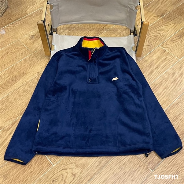 Áo nỉ lông kéo khóa nửa màu xanh navy, cổ đứng lót vàng viền đỏ, logo nhỏ ở ngực, trải trên ghế xếp