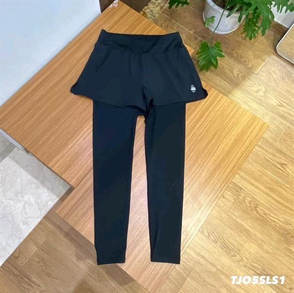 Quần legging liền váy short màu đen, trải phẳng trên mặt bàn gỗ, logo nhỏ ở gấu short