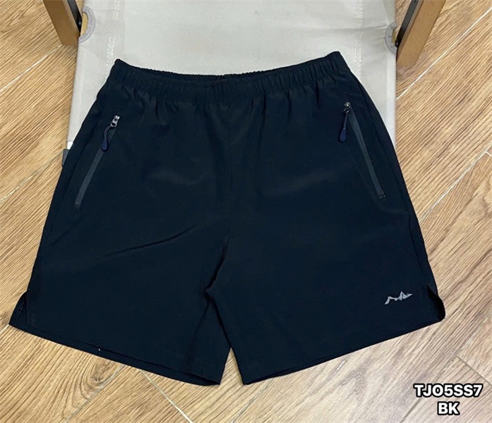Quần short đen trải phẳng mặt trước, cạp chun, hai túi khoá kéo hai bên, logo in nhỏ ở ống quần