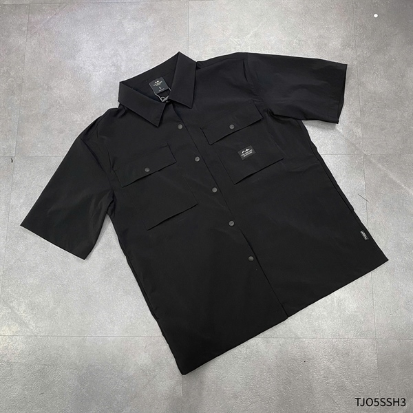 Black short-sleeve shirt laid flat, front view, with point collar, snap buttons and two flap chest pockets with small patch