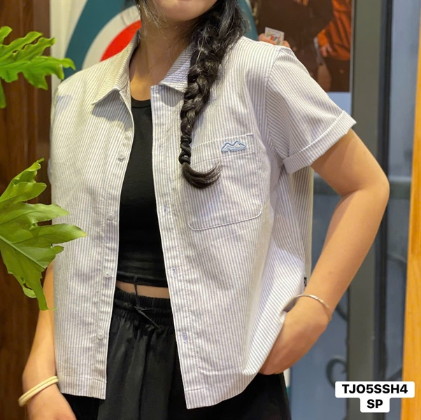 Woman in a cropped blue-and-white pinstripe short-sleeve shirt with embroidered logo on the chest pocket and rolled cuffs