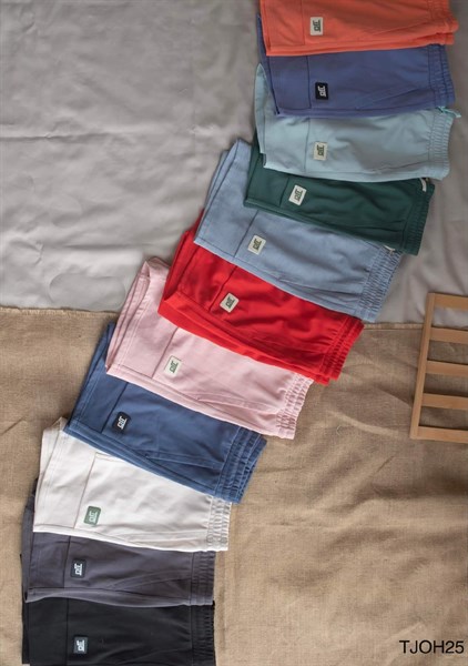 Nhiều quần short gấp xếp chéo đủ màu: cam, tím, xanh, đỏ, hồng, trắng, xám, đen trên nền vải bố
