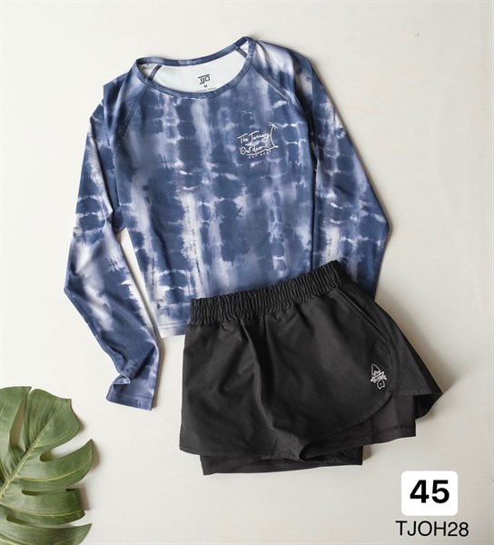 Navy and white tie-dye long-sleeve cropped top laid flat with layered black shorts beside a green leaf