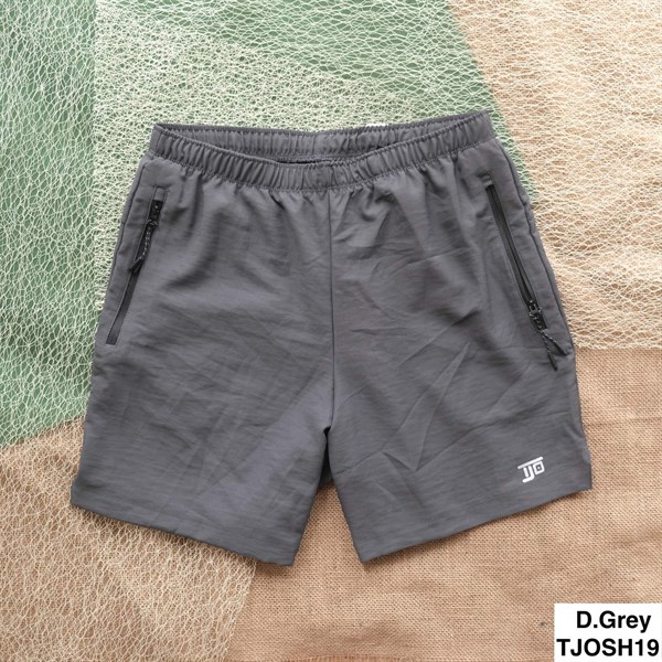 Dark grey shorts laid flat on netting and burlap, featuring an elastic waist, two zip pockets and a small leg logo